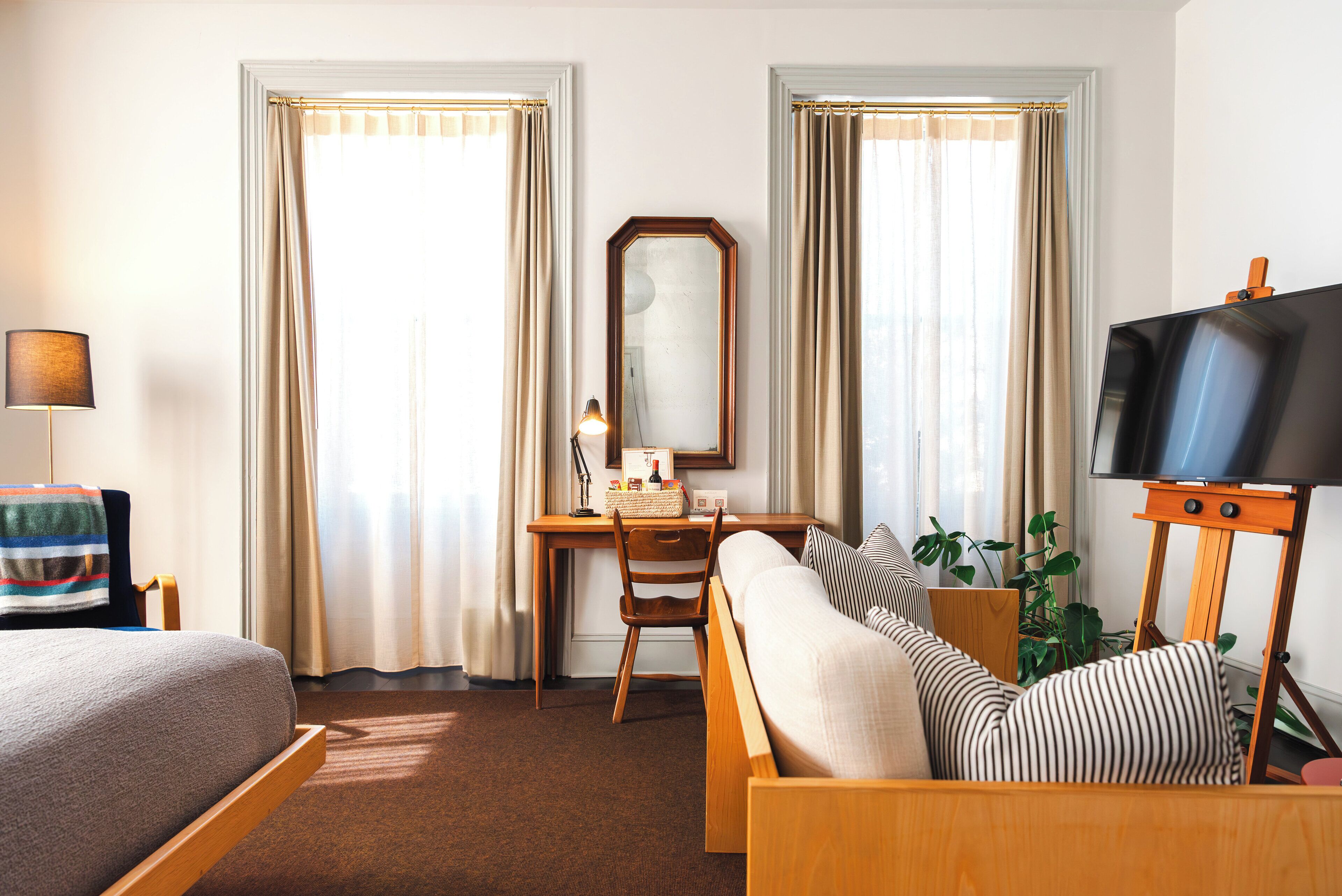 A hotel room with a bed, a desk with a chair, a television on a stand, and a large window with curtains.