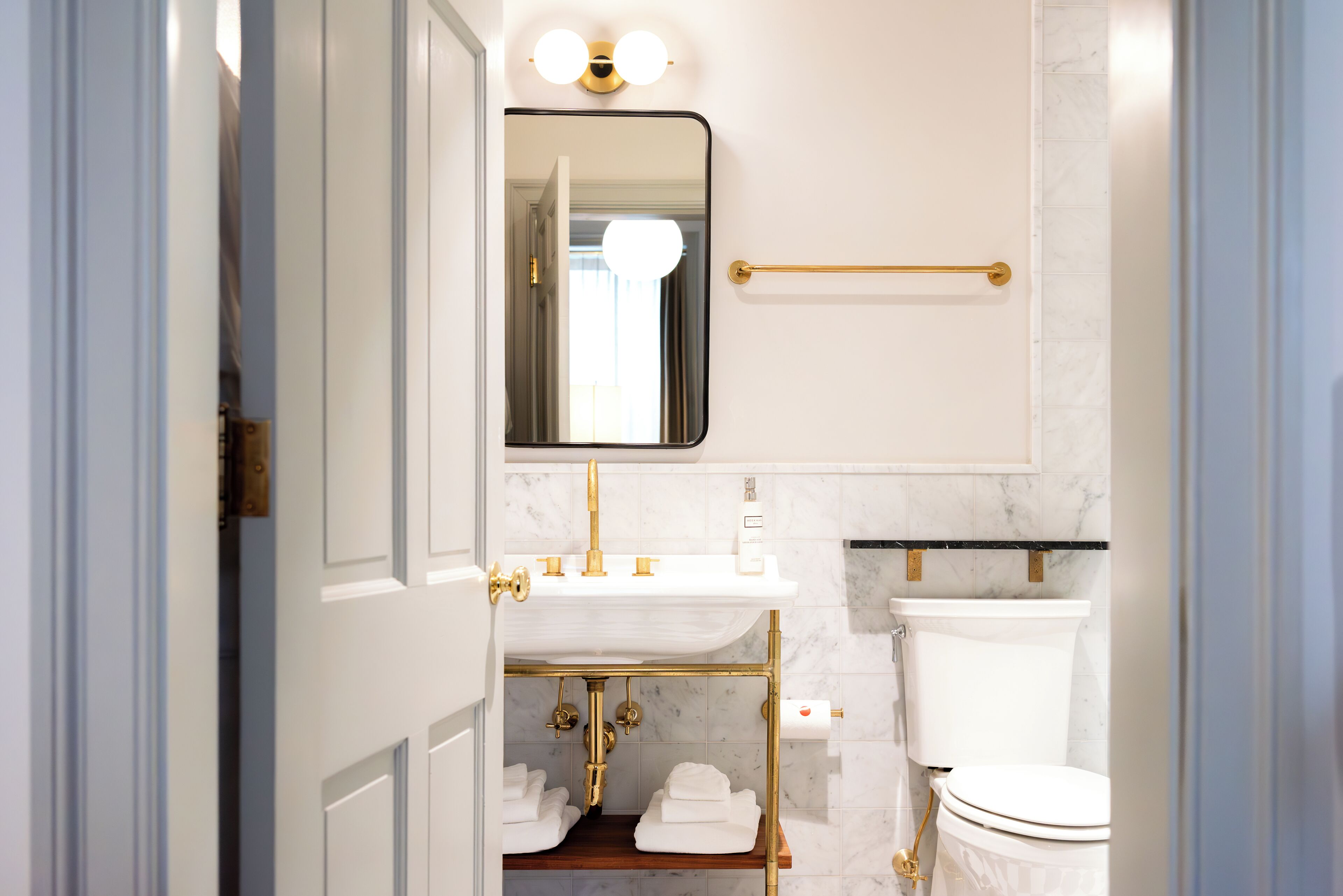 A bathroom with a white sink, gold fixtures, a mirror, and a toilet.