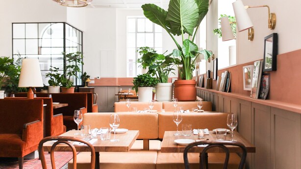 Een restaurant met oranje stoelen, witte tafelkleden en potplanten.