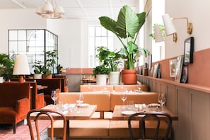 Un restaurante con asientos color naranja, manteles blancos y plantas en macetas.