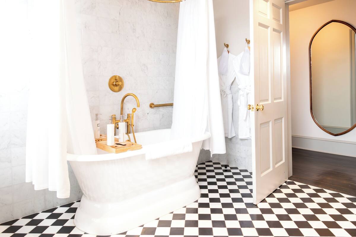 A bathroom with a white bathtub, gold fixtures, and a checkered floor.