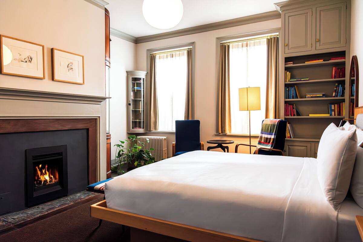 A hotel room with a fireplace, a bed, a bookshelf, and a window with curtains.
