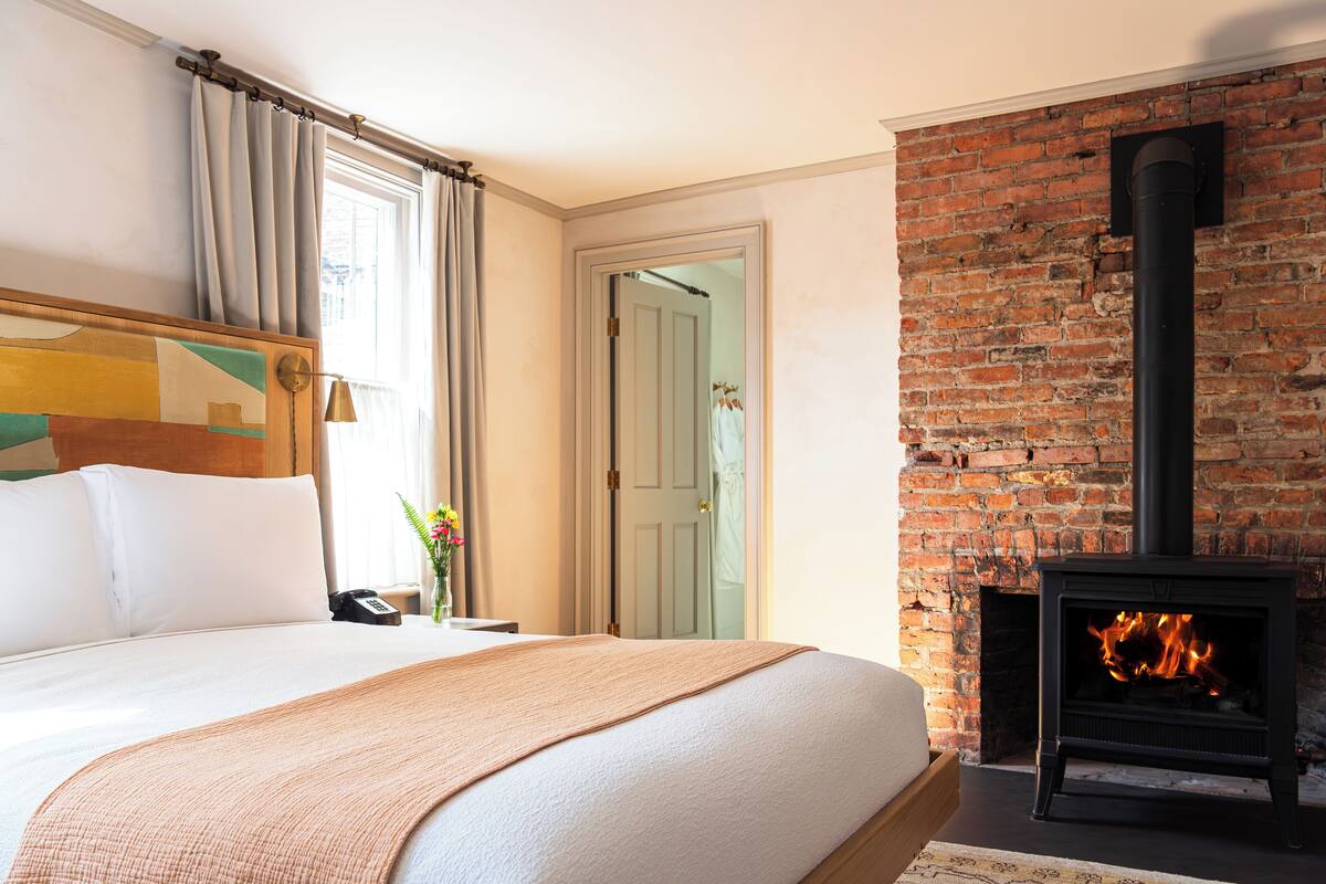 A hotel room with a large bed, a brick fireplace, and a view of a door.