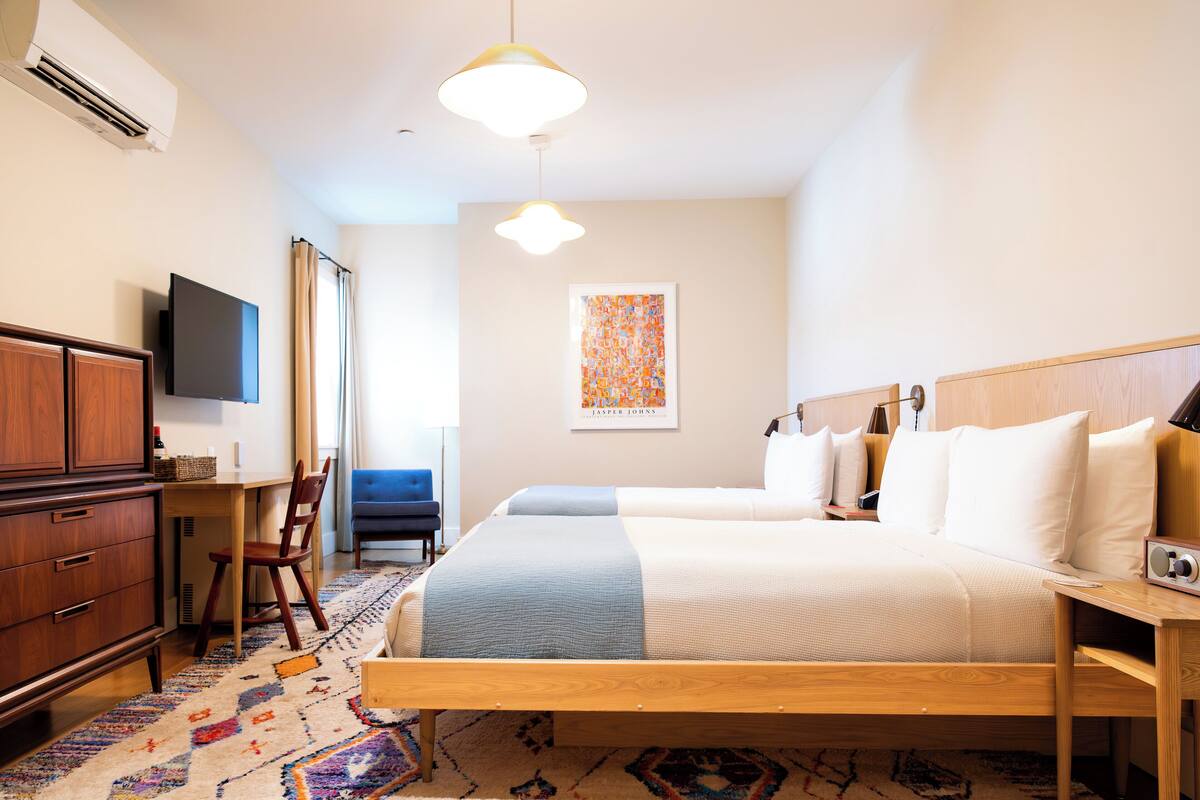 A hotel room with a bed, a desk, a chair, a television, and a painting on the wall.