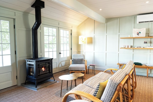 Una sala acogedora con estufa de leña, muebles de mimbre y una estantería.