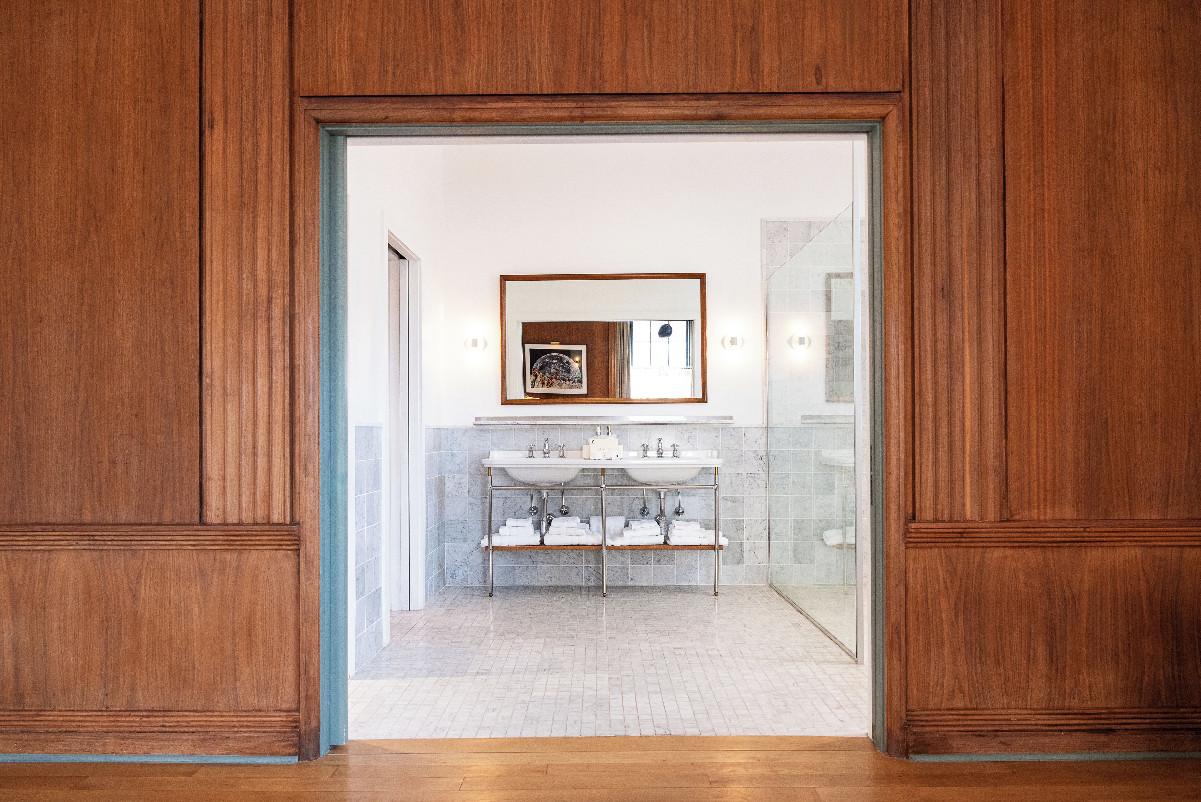 A wooden-framed doorway leading to a bathroom with a white sink and a framed picture above it.