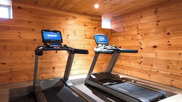 Dos cintas de correr con pantallas digitales en una habitación con paredes de madera y techo inclinado.