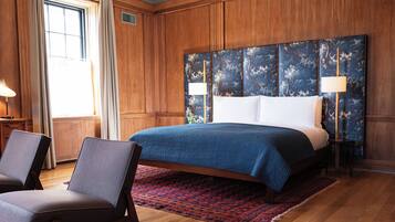 Une chambre d’hôtel avec un grand lit, deux chaises, une tête de lit en bois et un tapis rouge à motifs.