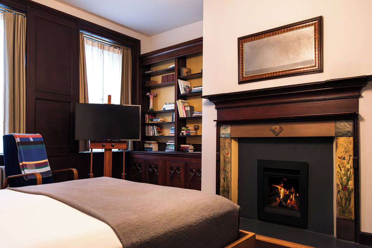 A hotel room with a bed, a television, a fireplace, and a bookshelf.