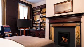 A hotel room with a bed, a television, a fireplace, and a bookshelf.