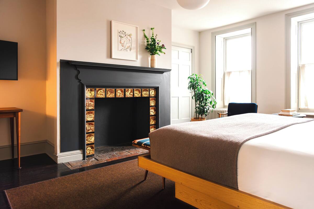 A bedroom with a large bed, a fireplace, a potted plant, and a window.