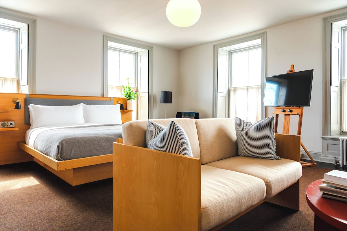 A modern hotel room with a bed, sofa, TV, and a small table.