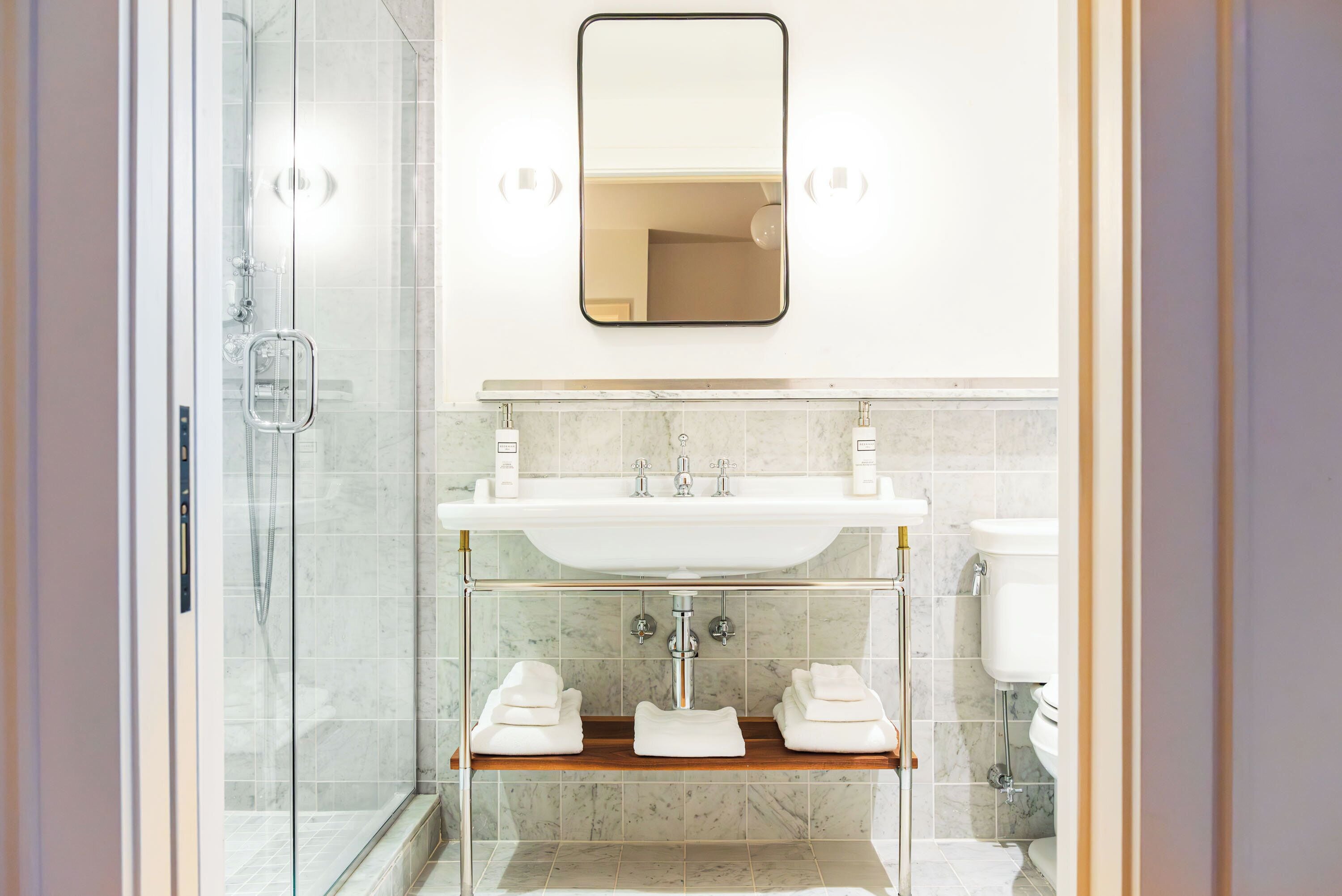 A modern bathroom with a glass shower enclosure, a white sink with a marble countertop, and a mirror above the sink.