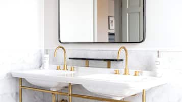 Un baño con dos lavamanos, accesorios dorados y un salpicadero de mármol.