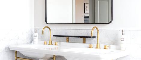 A bathroom with two sinks, gold fixtures, and a marble backsplash.