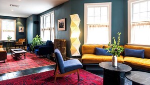 Een woonkamer met een rood design vloerkleed, een blauwe fauteuil, een gele bank en een zwarte salontafel.