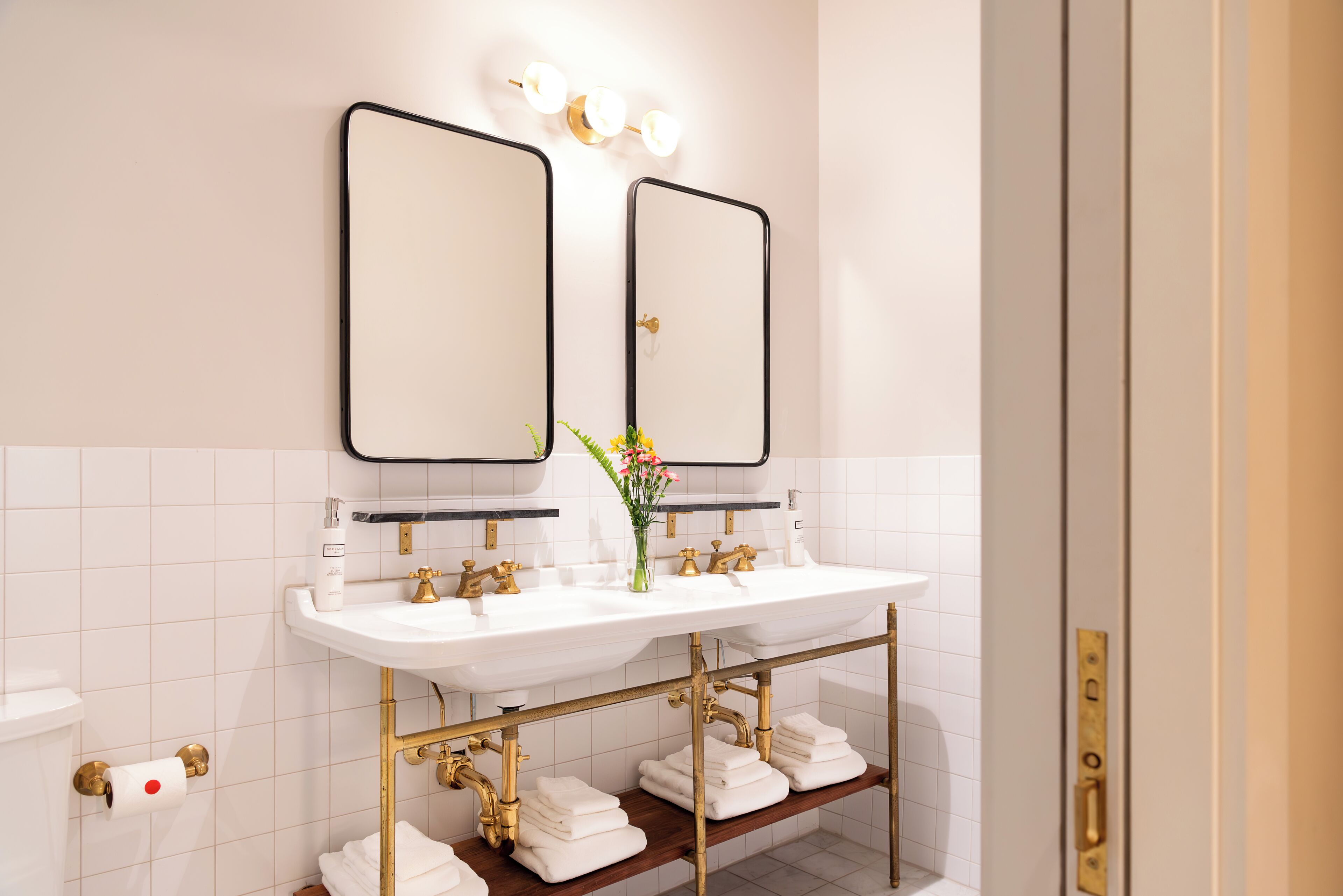 A bathroom with two sinks, a mirror, and a shelf with towels.