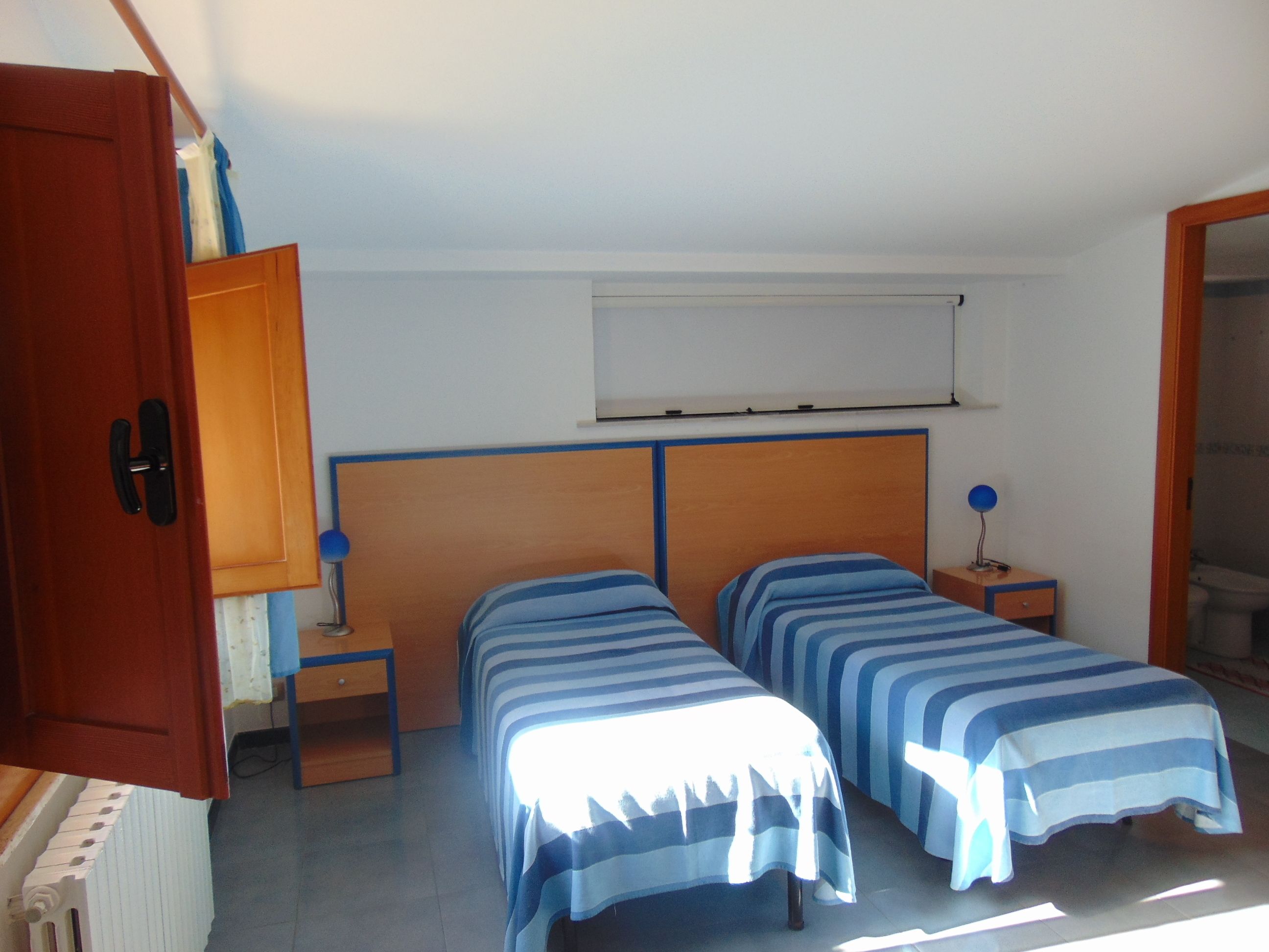 Un dormitorio con dos camas individuales, un cabecero de madera, una mesita de noche pequeña con lámpara y un radiador.