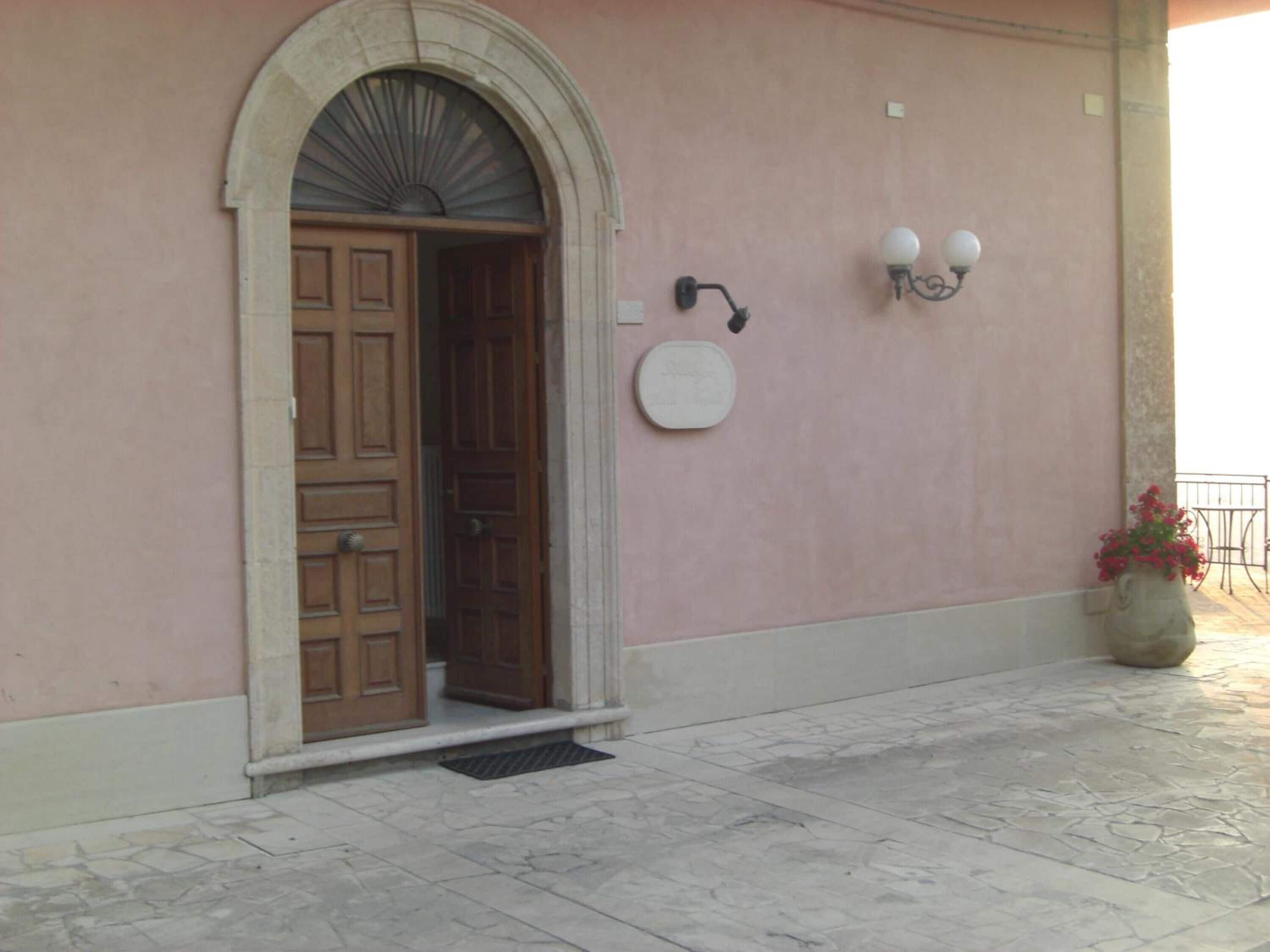 Una entrada de edificio con puerta de madera, arco de piedra, lámpara de pared y planta en maceta.