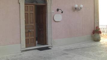Una entrada de edificio con puerta de madera, arco de piedra, lámpara de pared y planta en maceta.