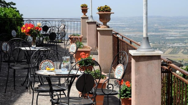 An outdoor terrace with tables and chairs, potted plants, and a view of the landscape. - Albergo villa nobile (Chiaramonte Gulfi)