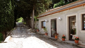 A building with a tiled roof, potted plants on the porch, and a stone pathway leading to it. - Albergo villa nobile (Chiaramonte Gulfi)