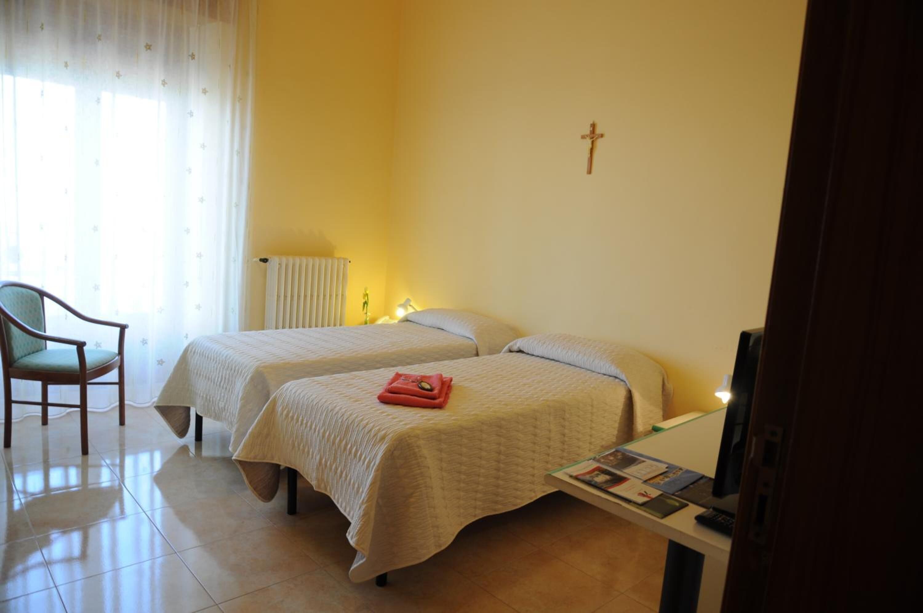 Une chambre d’hôtel avec deux lits, une chaise, un bureau avec un ordinateur et un radiateur.