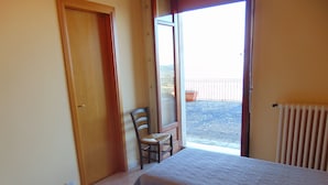 A room with two beds, a chair, a door, and a view of a balcony with a potted plant. - Albergo villa nobile (Chiaramonte Gulfi)