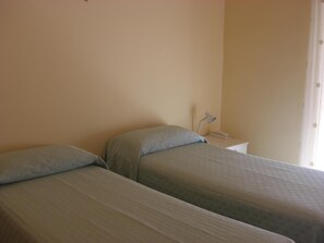A simple room with two beds, a bedside table with a lamp, and a curtain. - Albergo villa nobile (Chiaramonte Gulfi)