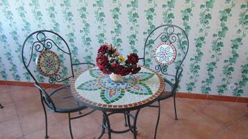 A round table with a mosaic top, two chairs with decorative backs, and a vase with flowers.