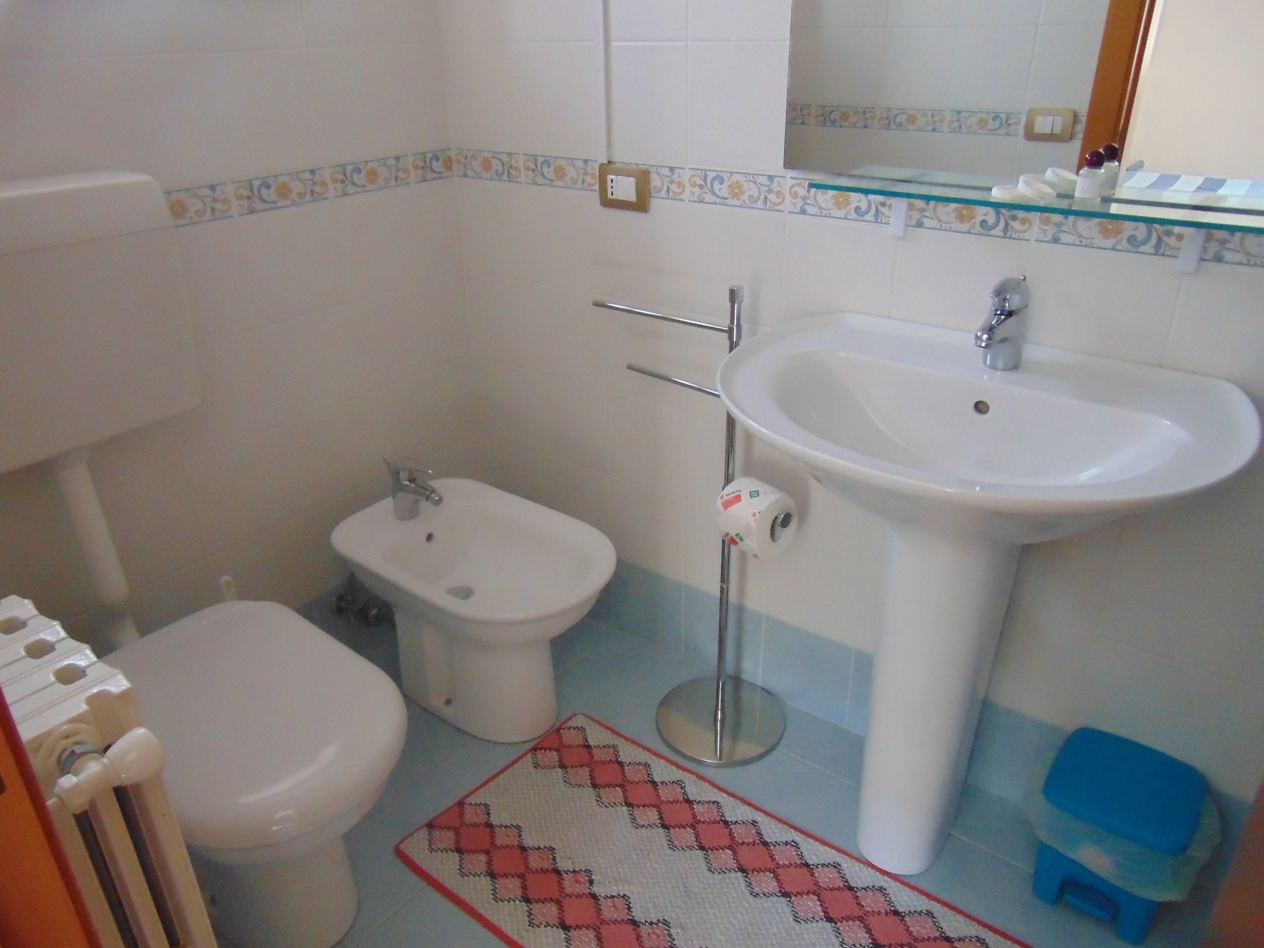 A bathroom with a toilet, bidet, sink, and a small blue stool.