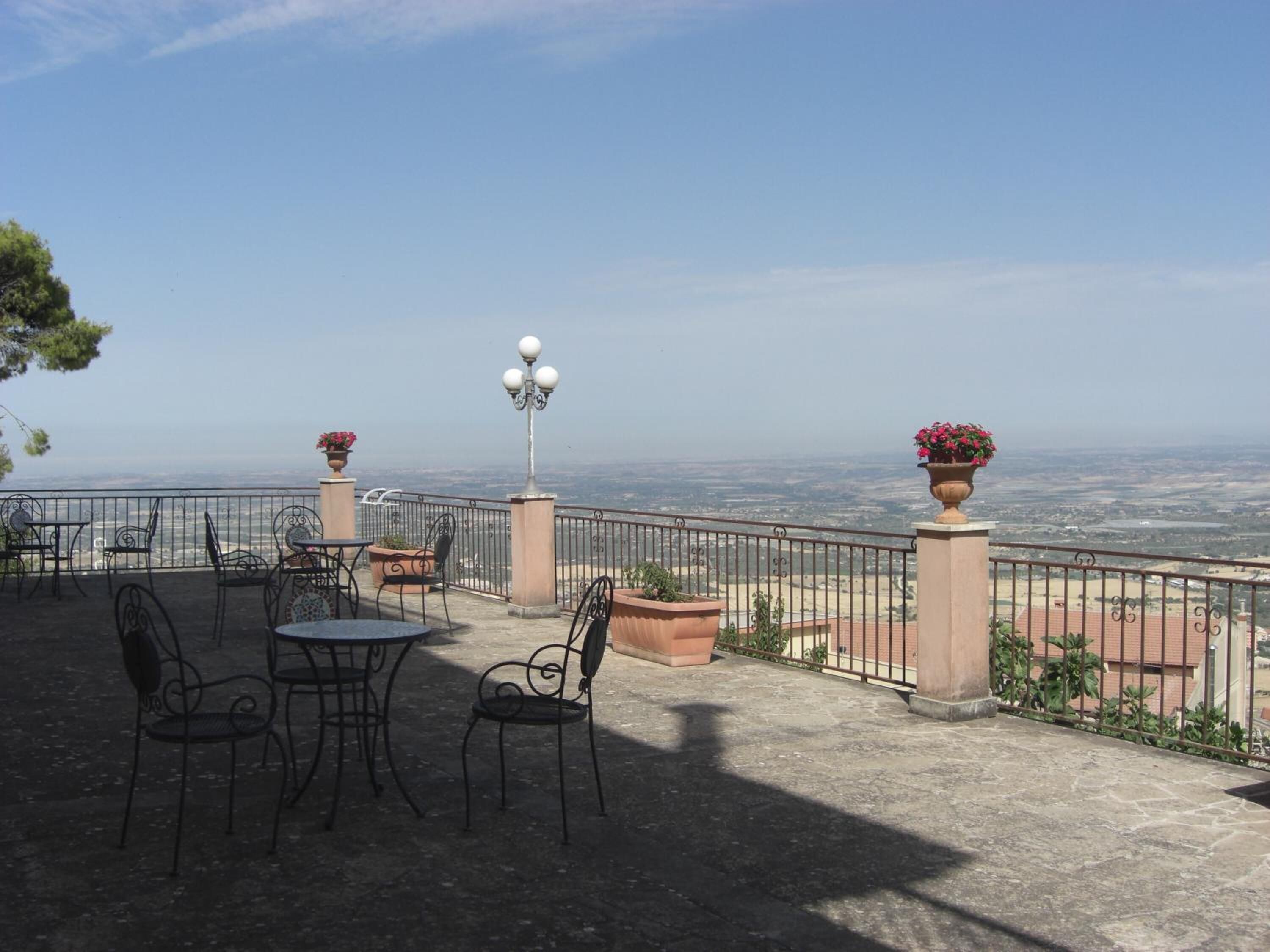 Une terrasse extérieure avec une table et des chaises, une lampe et des pots de fleurs.