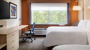 Een hotelkamer met een groot bed, een bureau met stoel, een televisie en een raam met uitzicht op bomen.