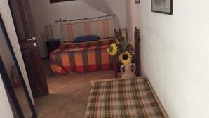 A small, dimly lit room with a bed, a chair, and a vase with sunflowers. - La Valle Dei Corbezzoli (Sassari)