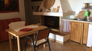 A cozy kitchen with a wooden table, a chair, a fireplace, and a sink. - La Valle Dei Corbezzoli (Sassari)