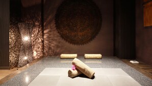 A spa room with a large circular wall decoration, a textured wall panel, and two rolled towels on the floor. - Hotel The Lotus Bali - Adult Only (Kawasaki)