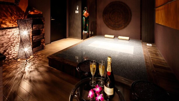 A room with a large wooden table, two glasses of champagne, and a bottle on a tray with flowers. - Hotel The Lotus Bali - Adult Only (Kawasaki)