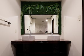 A bathroom with two sinks, a mirror, and a green plant wall. - Hotel The Lotus Bali - Adult Only (Kawasaki)