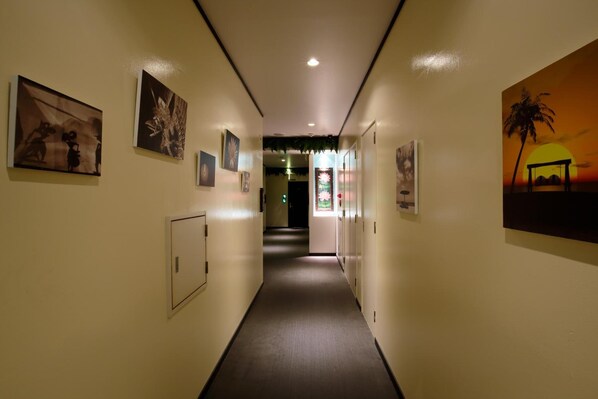 Un couloir aux murs ornés d’œuvres d’art, doté d’un sol recouvert de moquette et d’une porte au bout.