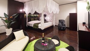 A bedroom with a canopy bed, a sitting area with a glass table, and a green rug. - Hotel The Lotus Bali - Adult Only (Kawasaki)