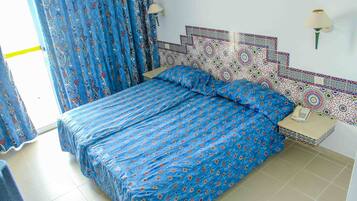 A room with a bed, a nightstand, a lamp, and patterned curtains.