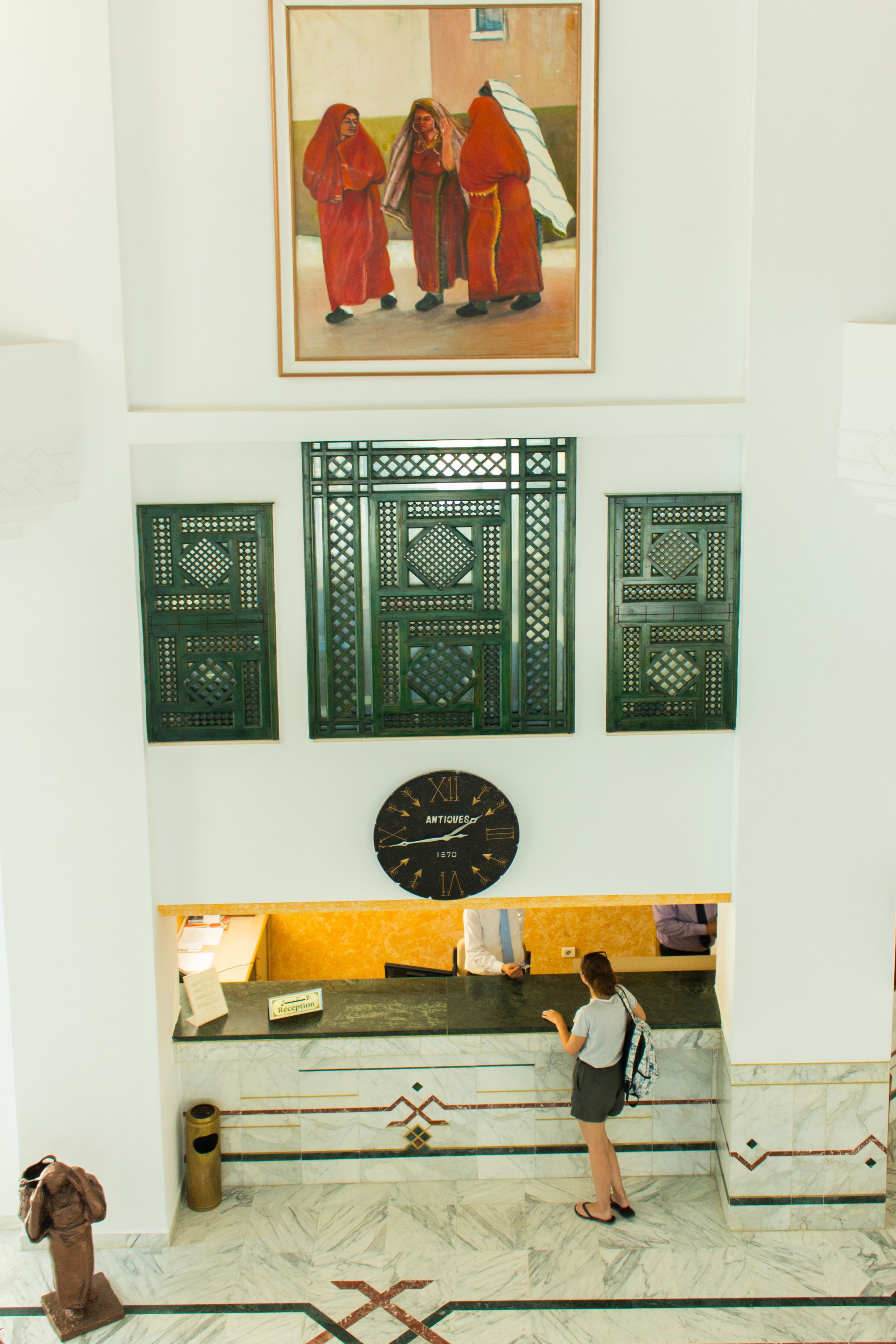 A reception area with a clock, a framed painting, and traditional green lattice panels.
