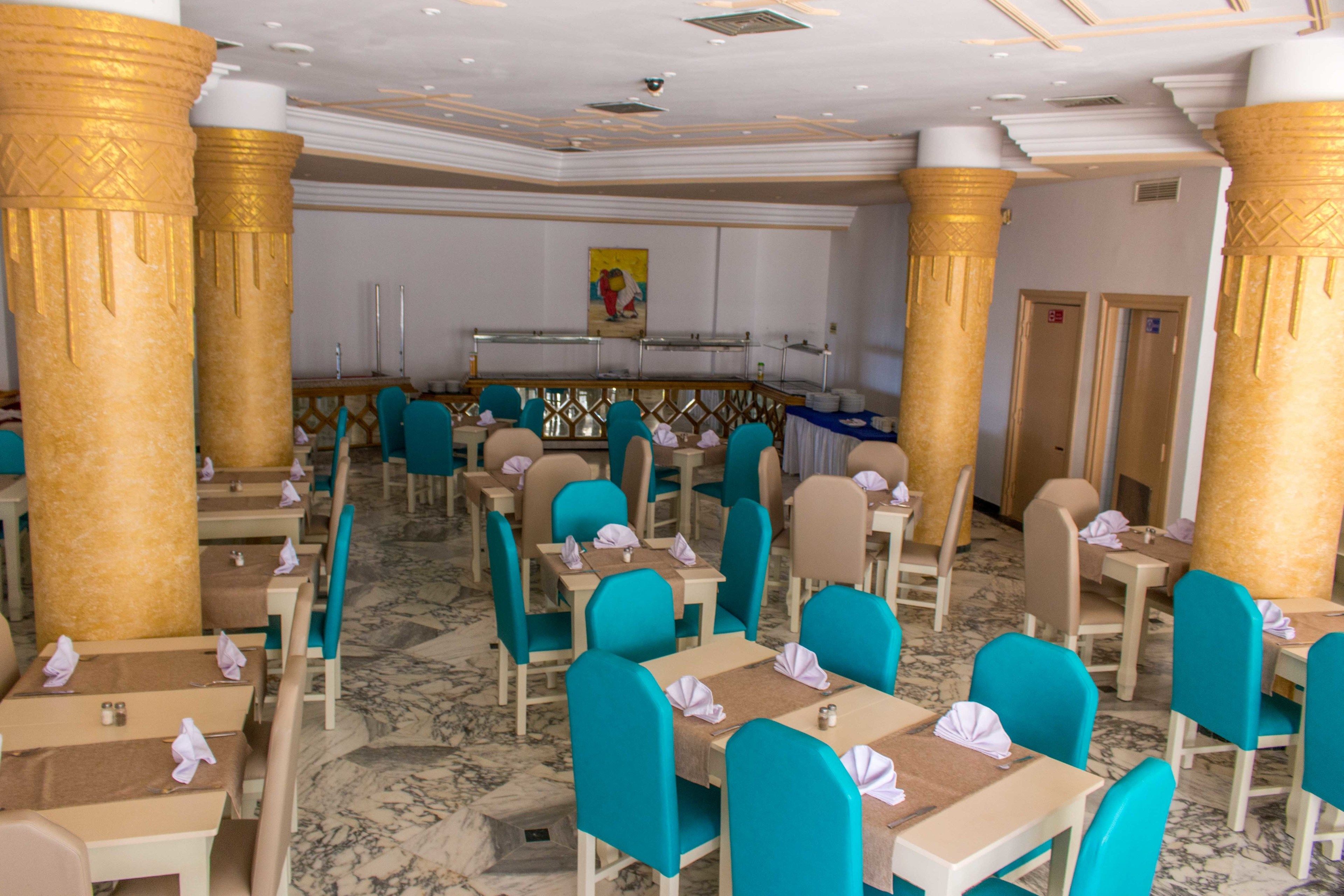 A restaurant with turquoise chairs and tables, marble flooring, and golden columns.