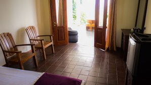 Una habitación con una cama, dos sillas de madera, una mesita, un televisor y una puerta que da a un espacio al aire libre.