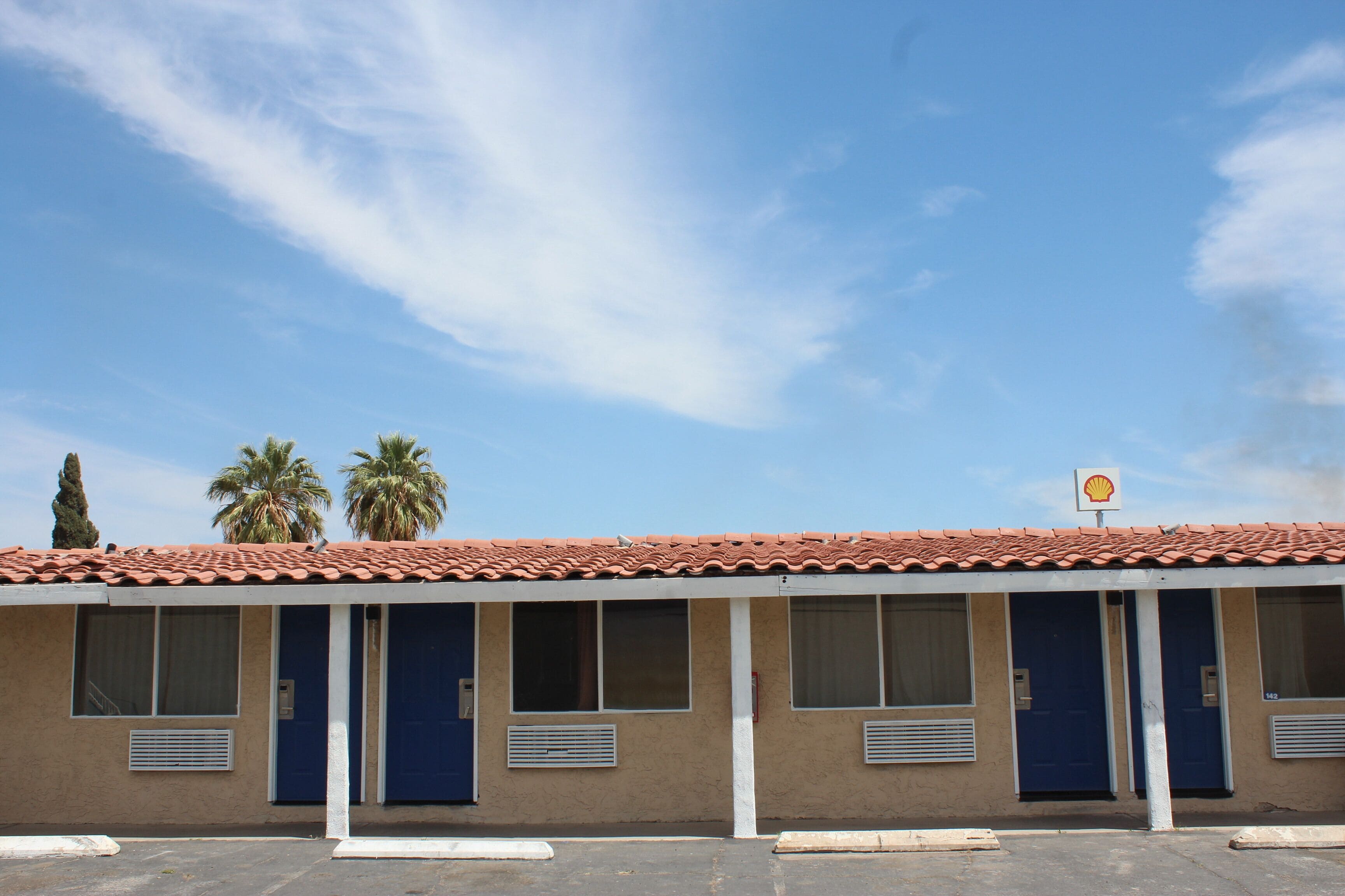 A motel with a red-tiled roof, blue doors, and a Shell sign.