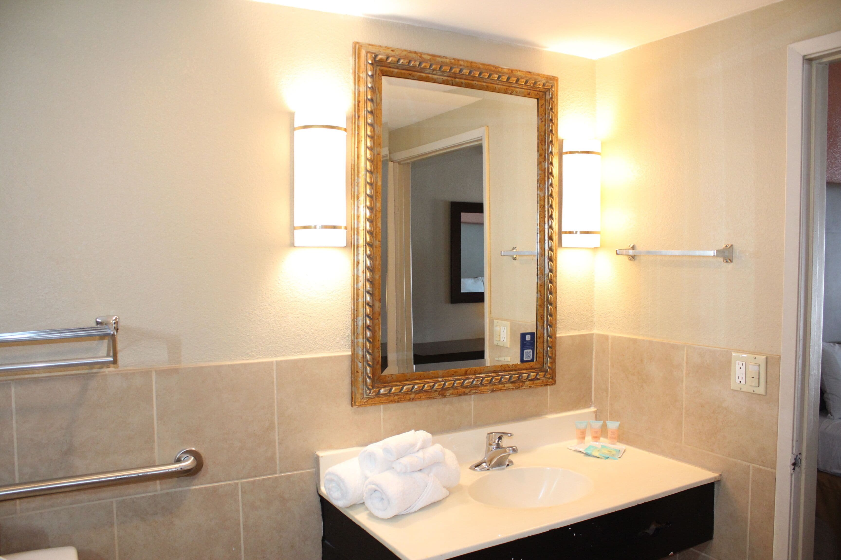 A bathroom with a large mirror, a sink, and a towel rack.