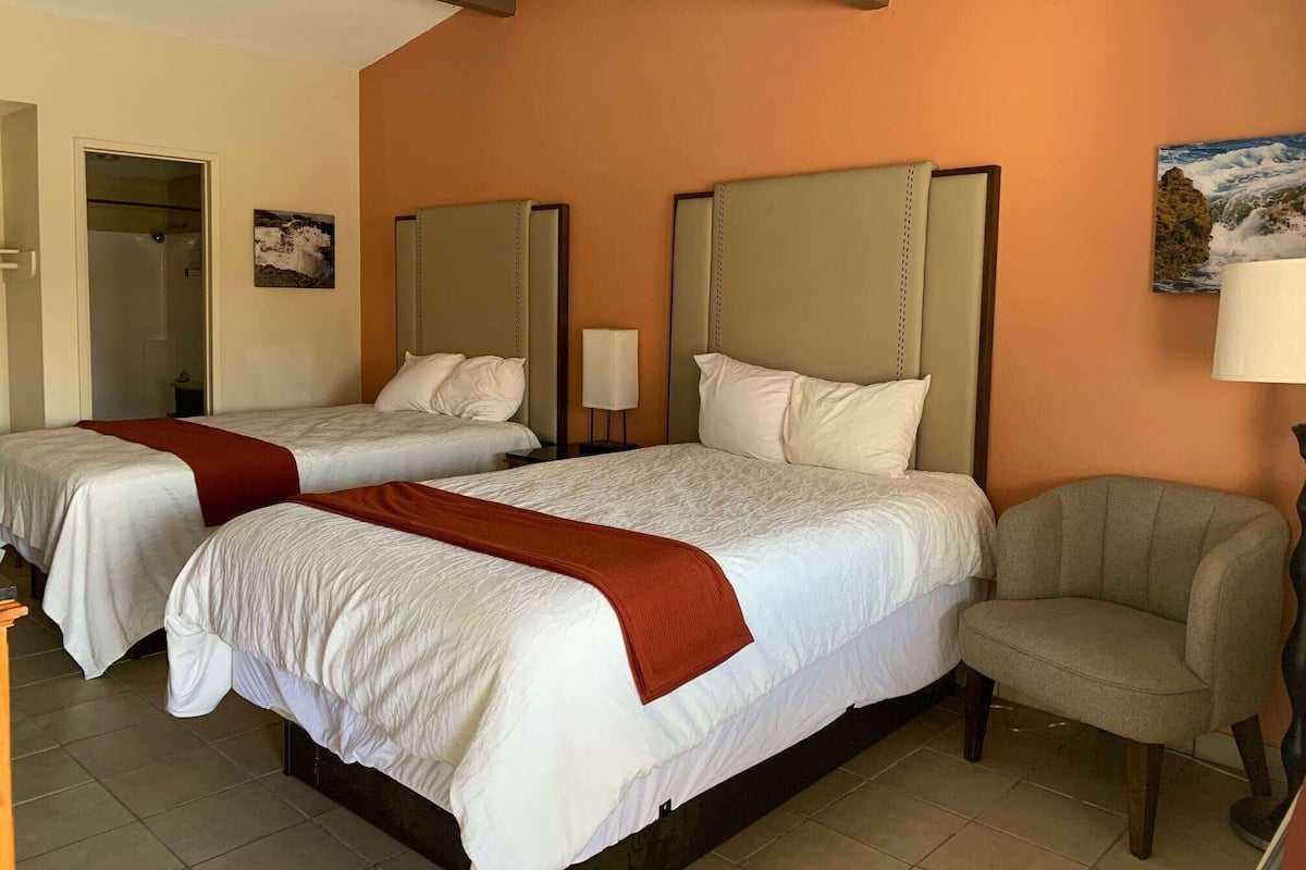 Una habitación de hotel con dos camas, una silla y un cuadro en la pared.