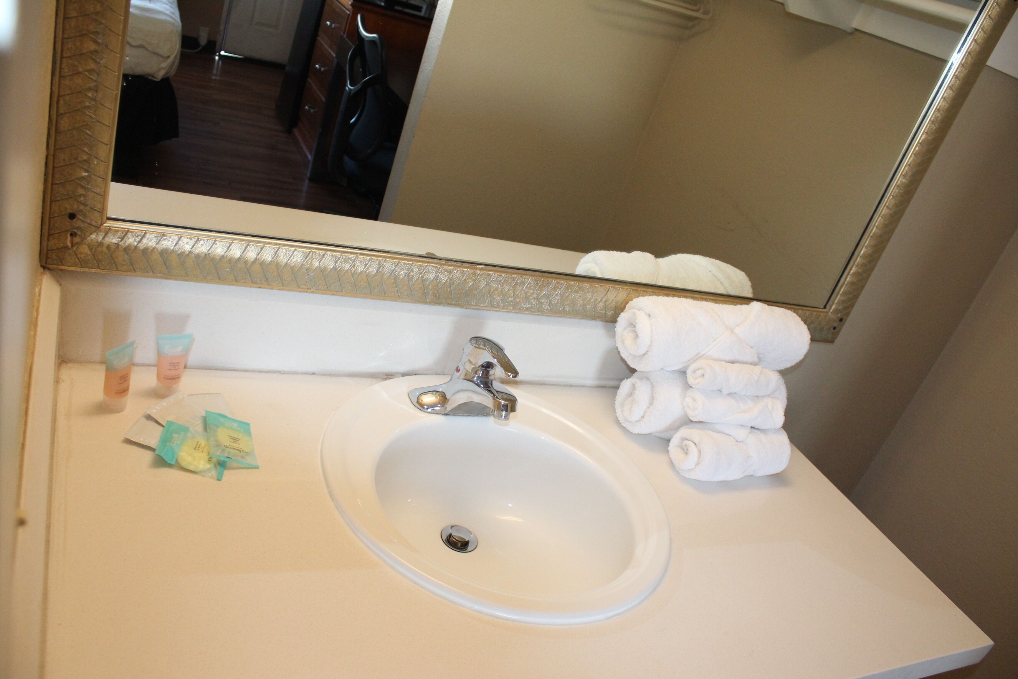 A bathroom with a white sink, a mirror, and a stack of white towels.