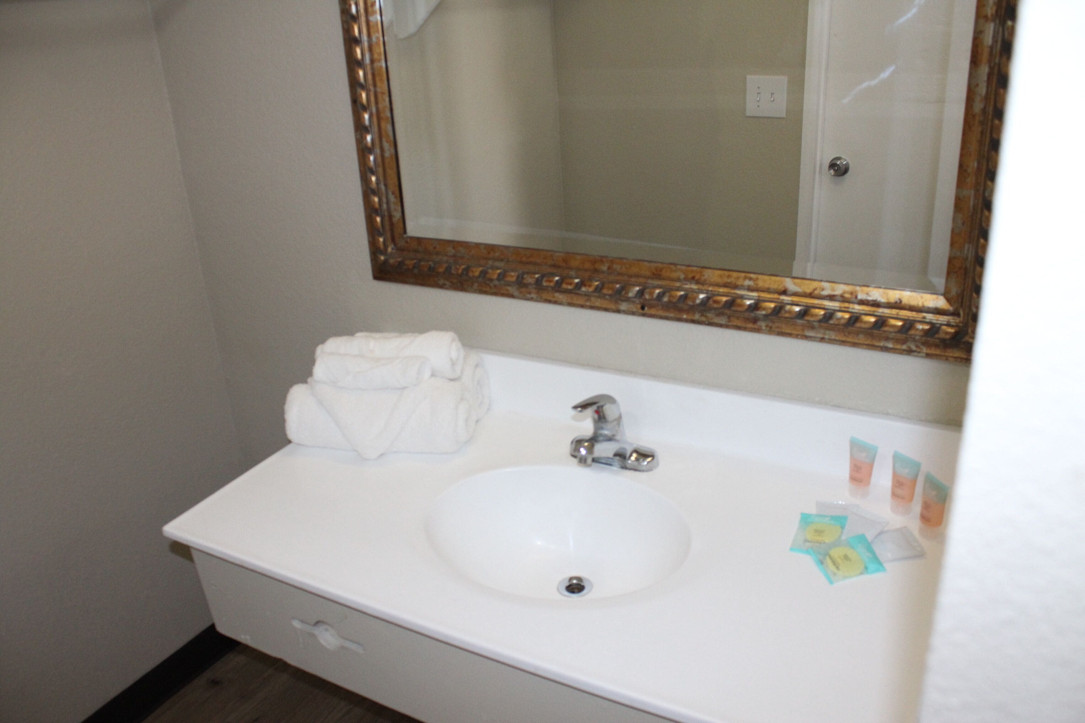 A white bathroom sink with a gold-framed mirror, a towel, and toiletries.