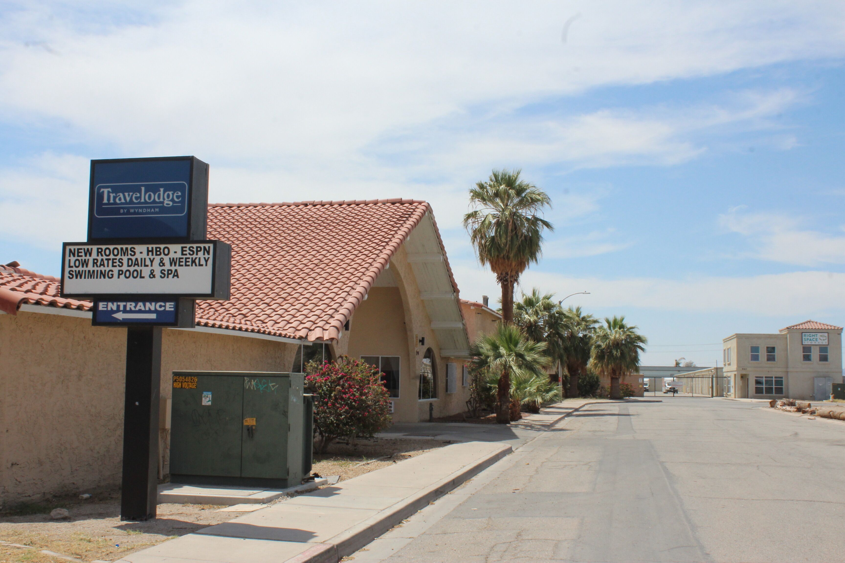 A Travelodge hotel entrance with a sign indicating amenities like new rooms, HBO, ESPN, low rates, a swimming pool, and a spa.